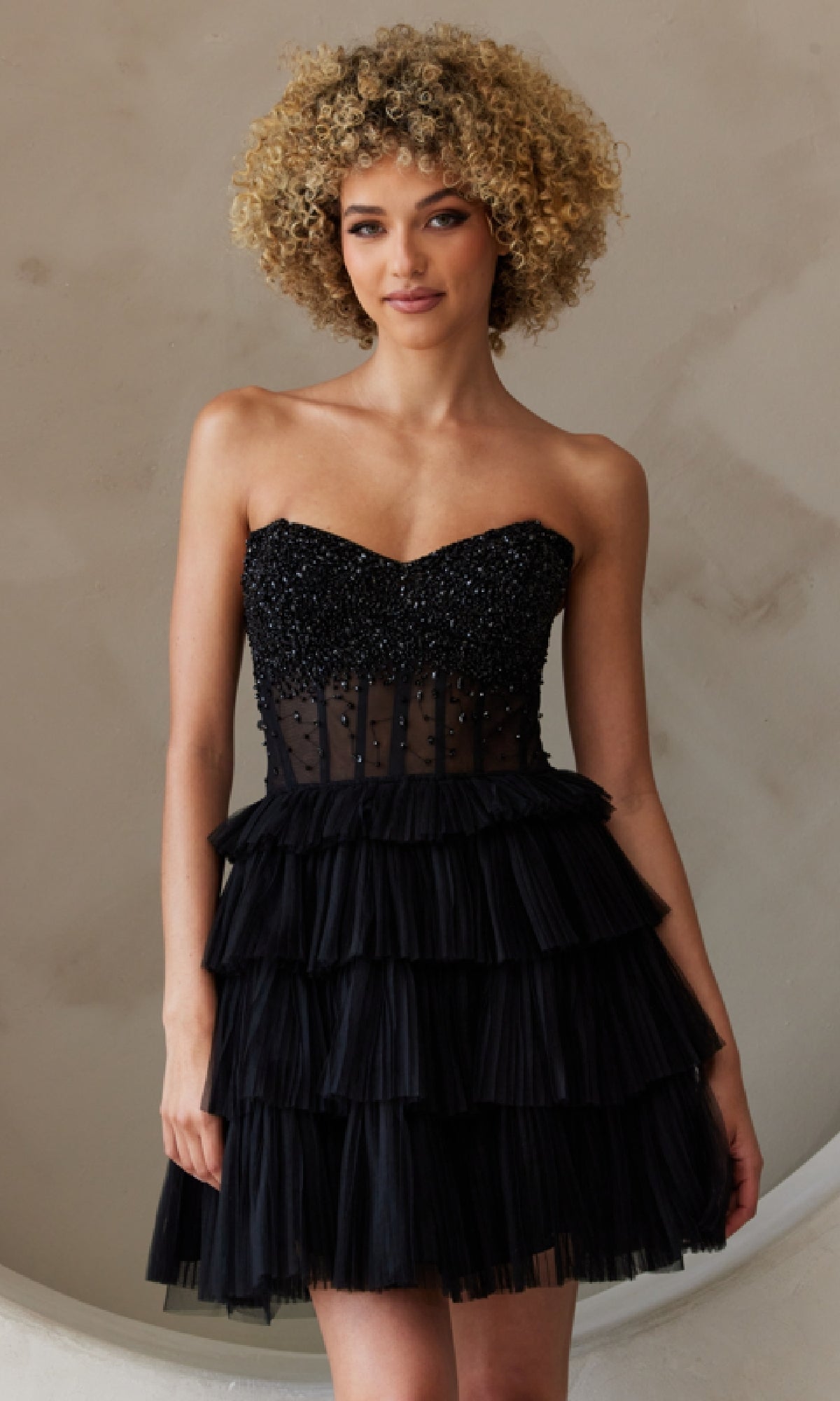 A person poses against a neutral background wearing the Strapless Short Ruffled A-Line Hoco Dress BZ9999S, featuring a beaded bodice and tiered skirt.
